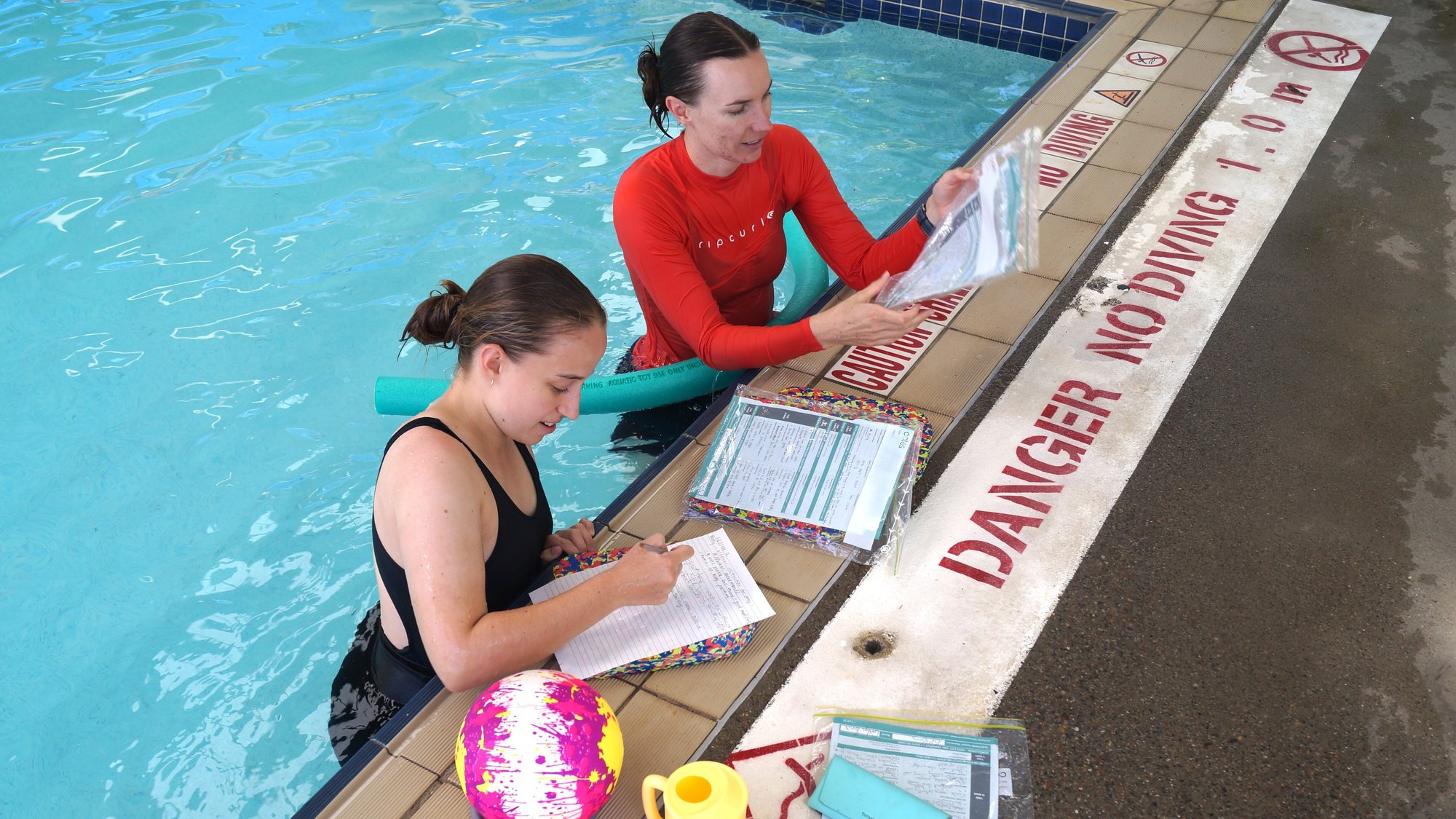 Swim teachers completing assessment documentation poolside during AUSTSWIM accredited training in New South Wales.