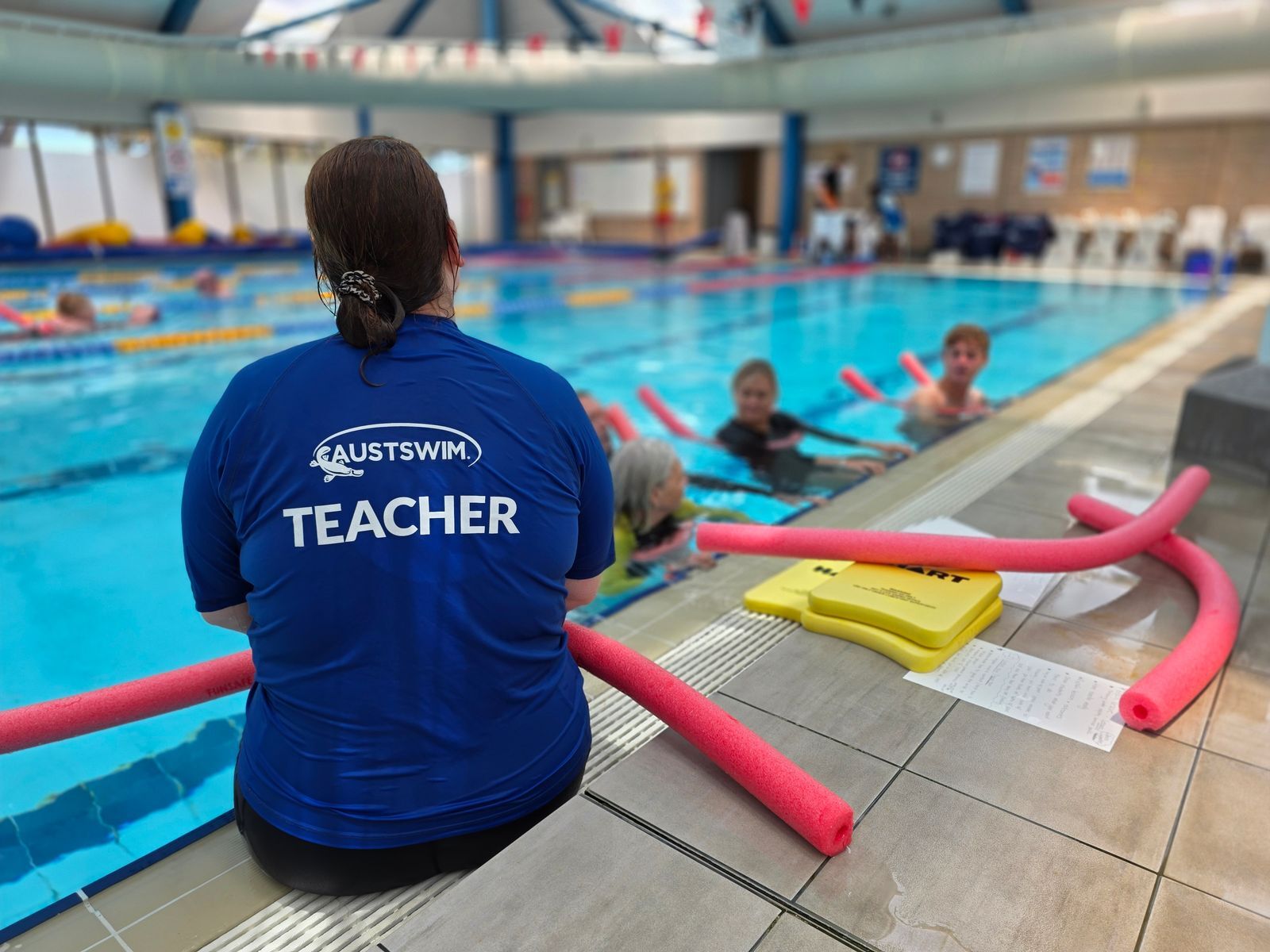 AUSTSWIM teacher besides a pool supporting students.