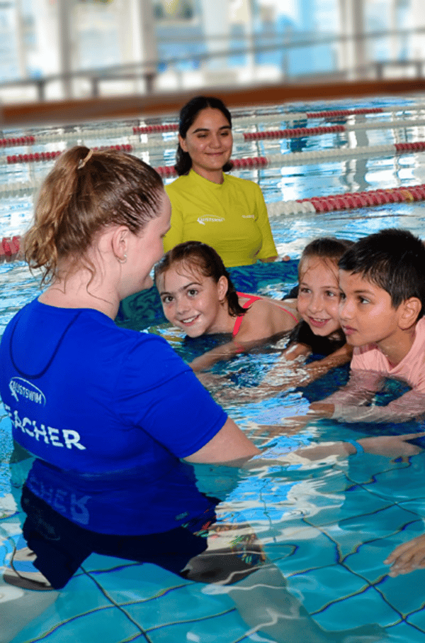 Image of two AUSTSWIM teachers in a pool teaching children who are smiling.