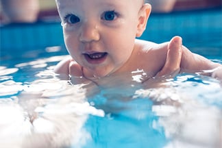 Baby being held by a swim teacher in a swimming pool.