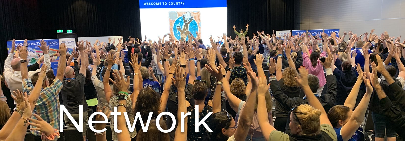 AUSTSWIM Network banner image. Group of event attendees standing with their hand in the air at an AUSTSWIM event. The word Network is layered over the top of the image.